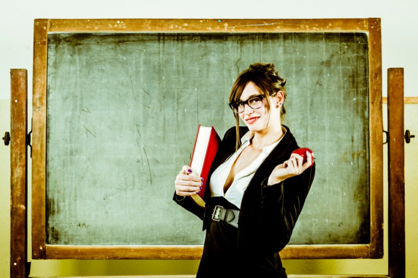 Big breasted teacher stands in front of a green blackboard