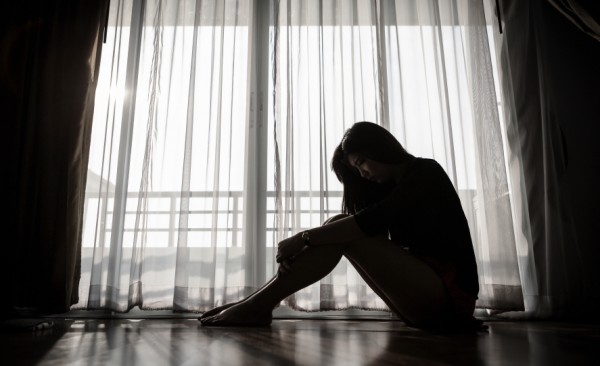 Silhouette of a woman with knees in hands next to a windiow