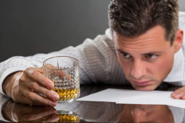 Man with head on table looks at shot of whiskey