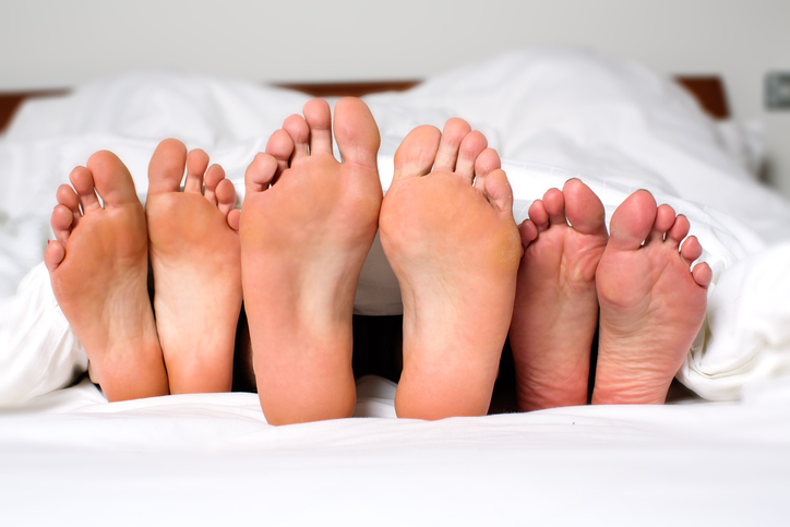 Humorous image of the bare feet of a man and two women in bed sticking out from under the bedclothes conceptual of a threesome, orgy, swingers or sexual cheating