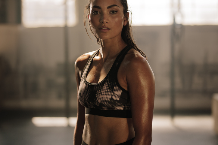 Strong and determined female in sportswear standing in the gym and looking at camera. Sportswoman after intense crossing training workout session in gym.