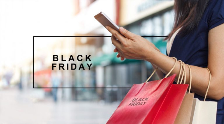 Black Friday, Woman using smartphone and holding shopping bag while standing on shopping mall background