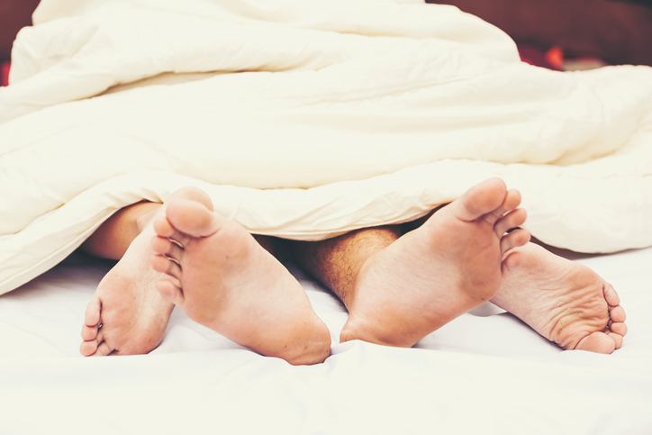 Close up of male and female feet on a bed - Loving couple having sex under white sheets in the bedroom - Concept of sensual and intimate moment of lovers - Vintage filter - Focus on male foot