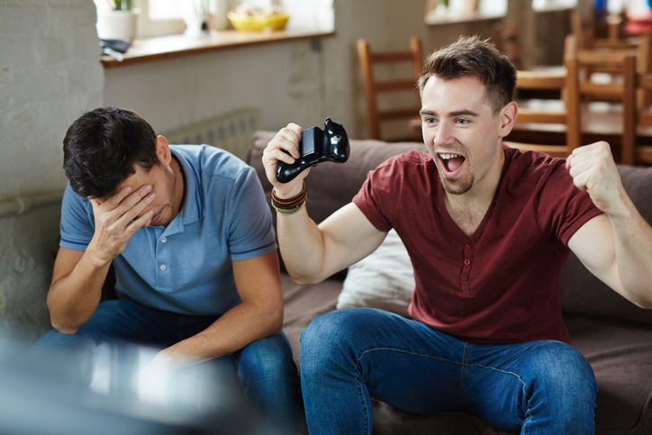 Ecstatic gameplayer expressing triumph with his defeated friend near by