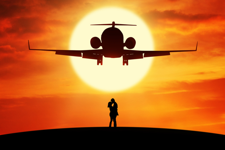Silhouette of young couple standing on the hill and kissing under a flying airplane at sunset time