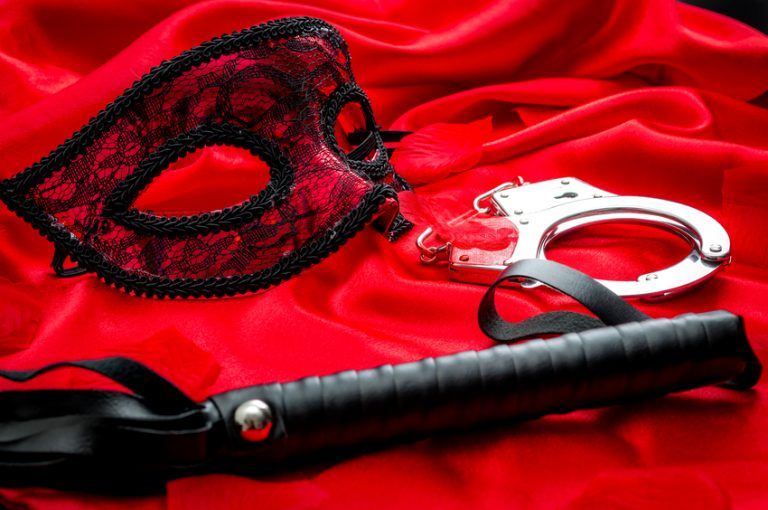 BDSM concept: flogger (whip), handcuffs and eyemask on red satin