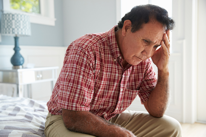 Depressed old man on edge of bed