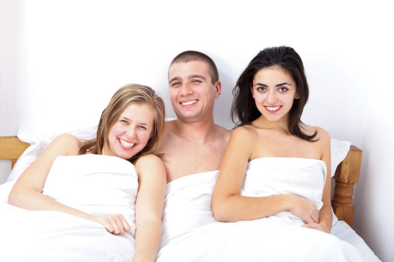 man in the middle of two women in bed