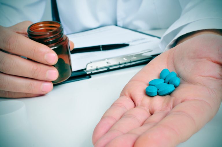 a doctor sitting in a desk with a pile of blue pills in his hand