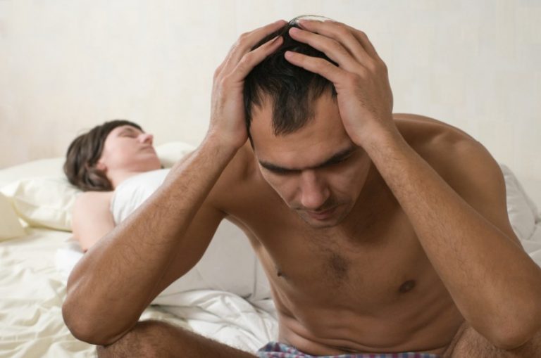 Man sits on the edge of bed stressed while woman sleeps