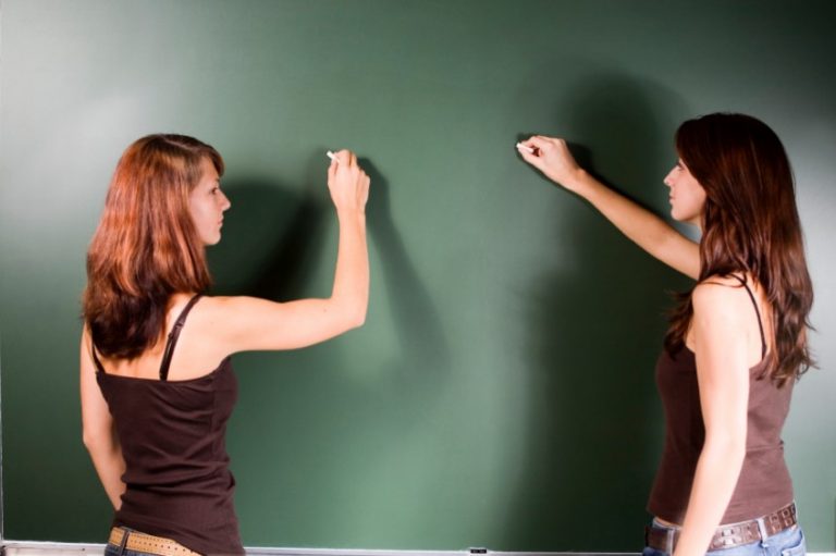Two young teachers write on a green blackboard